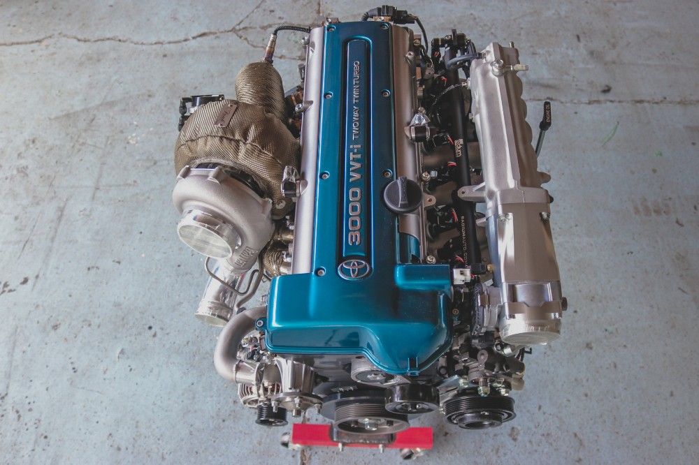 Toyota 2JZ-GTE twin turbo engine with teal valve cover sitting on an engine stand